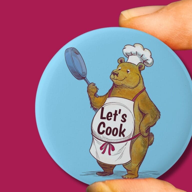 A pin badge with a bear in a chefs outfit, holding a frying pan
