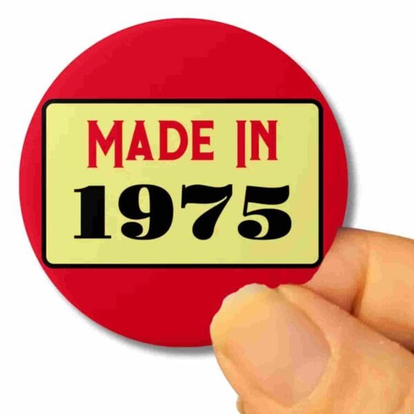 a hand holding a round badge that is mainly red in colour, with the words on it that say, 'made in 1975'